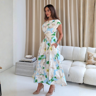 Woman in a floral dress standing in a living room with beige curtains and a white sofa.