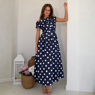 Woman wearing a navy blue dress with white polka dots in an indoor setting.