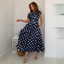 Load image into Gallery viewer, Woman wearing a navy blue dress with white polka dots in a minimalistic room.
