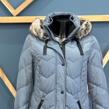 Load image into Gallery viewer, Blue puffer jacket with fur-lined hood on a mannequin against a geometric-patterned wall.
