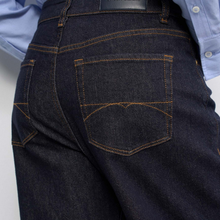Load image into Gallery viewer, Close-up back view of dark indigo denim jeans with orange contrast stitching, worn with a light blue button-up shirt.
