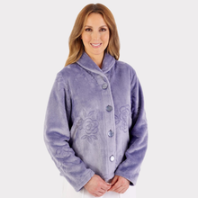 Load image into Gallery viewer, Model wearing a soft grey floral embossed fleece bedjacket, standing casually, showcasing the classic fit and cozy texture
