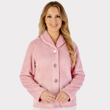 Load image into Gallery viewer, Model wearing a delicate pink floral embossed fleece bedjacket, highlighting the embossed floral design and comfortable loungewear style.
