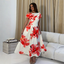 Load image into Gallery viewer, Woman wearing a white dress with red floral patterns in a living room setting.
