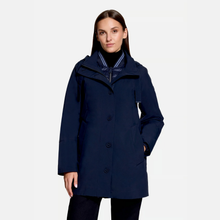 Load image into Gallery viewer, A woman modeling a navy blue mid-length coat with a high collar and front buttons, photographed against a light gray studio background.
