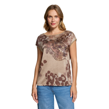 Load image into Gallery viewer, A woman modeling a short-sleeve beige top with a brown abstract floral pattern, paired with blue jeans, against a plain white background.
