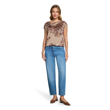 Load image into Gallery viewer, A woman modeling a short-sleeve beige top with a brown abstract print and blue jeans, standing against a plain white background.
