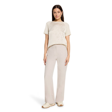 Load image into Gallery viewer, A woman modeling a light beige short-sleeve t-shirt with a subtle tonal graphic print and matching wide-leg trousers, standing against a plain white background.
