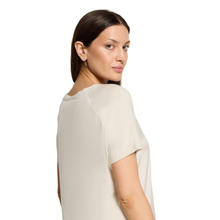 Load image into Gallery viewer, A woman with dark hair pulled back, wearing a short-sleeve cream-colored top, shown from a side-back angle against a plain white background.
