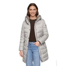 Load image into Gallery viewer, A woman modeling a light gray hooded puffer jacket with a brown knit top and blue jeans against a plain white background.
