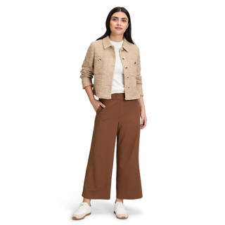 A woman modeling a cropped beige tweed jacket over a white top, paired with brown wide-leg trousers and white sneakers, on a solid white background.