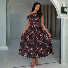 Load image into Gallery viewer, A woman modeling a dark brown off-the-shoulder midi dress with a brown and beige floral print, standing in a doorway.
