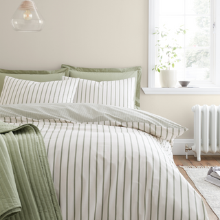 Bed with green and white striped bedding in a bright bedroom.