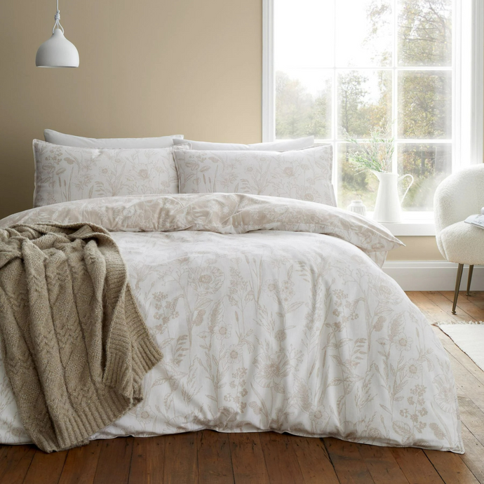 Neatly made bed with floral bedding in a bright room with large windows.