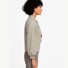 Load image into Gallery viewer, A woman shown in side profile wearing a light gray knit cropped sweater with a tie-neck detail and patterned plaid trousers, against a plain white studio background.
