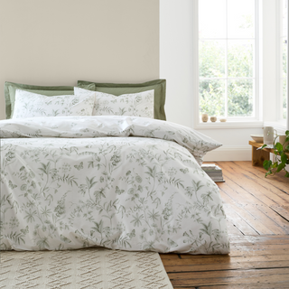 Floral bedding set on a bed in a bright bedroom with wooden floor.