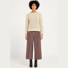 Load image into Gallery viewer, A model stands against a light gray studio background wearing a cream ribbed knit sweater, mauve wide-leg cropped trousers, and black ankle boots.
