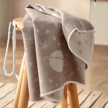 Load image into Gallery viewer, A soft taupe-gray blanket with a white celestial pattern of stars and a planet, draped over a wooden stool in a warm, softly lit room.
