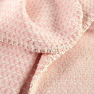 Close-up of a soft pink textured fabric with a cream-colored whipstitch border.