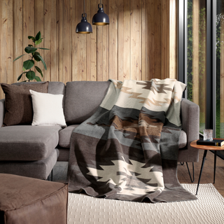 A patterned throw blanket draped over a gray sectional sofa in a modern living room with wood-paneled walls, pendant lights, and a small side table.
