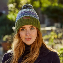 Load image into Gallery viewer, A woman wearing a multicolor knit beanie with a pom-pom and a green ribbed brim. The beanie has a small brown leather patch on the front with the brand name 'Pachamama'
