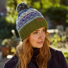 Load image into Gallery viewer, A woman wearing a multicolor knit beanie with a pom-pom and a green ribbed brim. The beanie has a small brown leather patch on the front with the brand name 'Pachamama'
