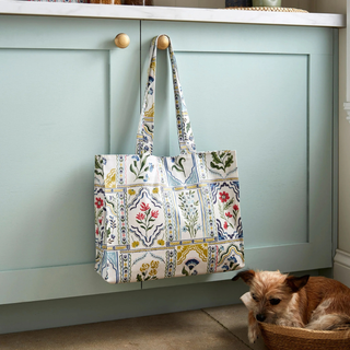 Colorful patterned tote bag hanging on a light green cabinet with a small dog sitting nearby.