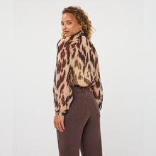 Load image into Gallery viewer, A woman wearing a beige leopard-print blouse with brown spots and dark brown trousers, photographed from the back against a plain white studio background.
