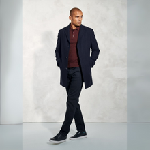 Load image into Gallery viewer, Man wearing a dark coat over a red shirt with black pants against a light gray background
