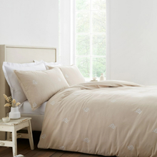 Load image into Gallery viewer, A beige bedding set with matching duvet cover and pillowcases featuring delicate white embroidered floral motifs, styled on a bed in a bright, minimalist bedroom.
