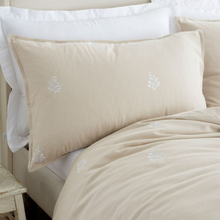 Load image into Gallery viewer, A beige pillow sham with delicate white embroidered floral motifs, styled on a bed with white pillows and a matching beige duvet cover.
