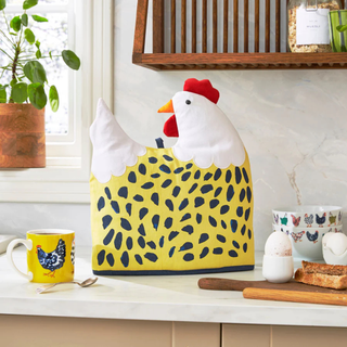 Chicken-shaped kitchen towel on a counter with a mug and bread in the background