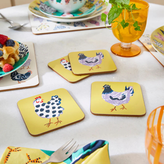 Set of yellow coasters with chicken designs on a table with waffles and a glass.