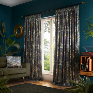 A living room with teal walls, and a full length window with full length curtains and a floral design. 