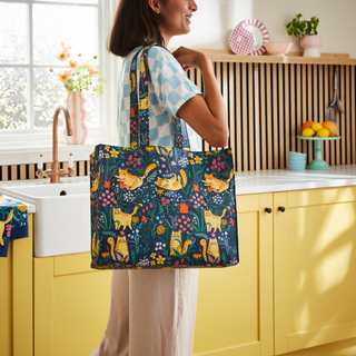 Woman holding a colorful tote bag with cat design in a kitchen.