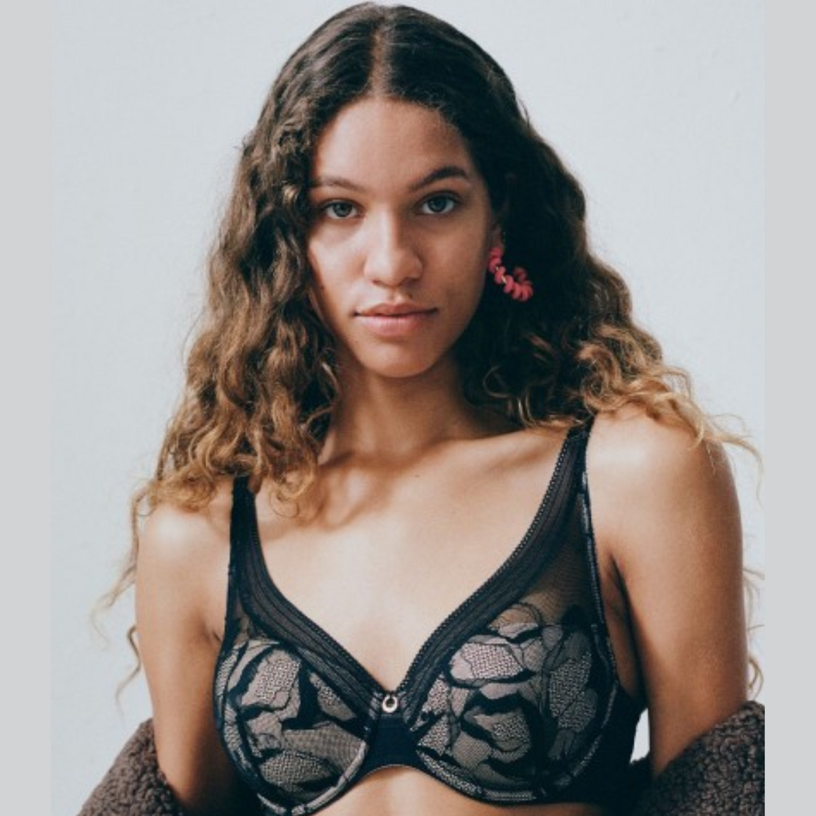 A model wearing a jacket shrugged off the shoulders while displaying the Chantelle True Lace Plunge Spacer Bra.