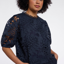 Load image into Gallery viewer, A woman wearing a navy blue lace top with floral cutout patterns and short puff sleeves, photographed against a clean white studio background.
