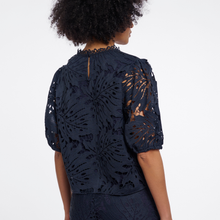 Load image into Gallery viewer, A woman viewed from the back wearing a navy blue lace top with short puff sleeves and an intricate floral cutout pattern, set against a plain white background.
