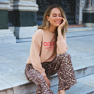 Woman wearing a beige sweatshirt with 'Chicago' text and leopard print pants sitting on steps.