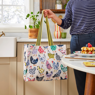 Person holding a tote bag with chicken design in a kitchen.
