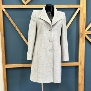 Gray coat on a mannequin against a blue wall with wooden geometric patterns