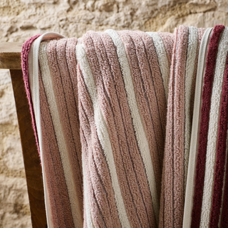 Striped towel with pink, beige, and red colors draped over a wooden surface against a stone wall background.