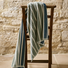 Load image into Gallery viewer, Striped towel draped over a wooden chair against a stone wall.
