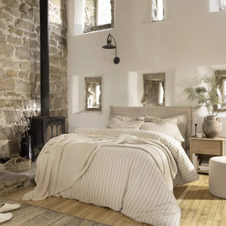 Cozy bedroom with stone wall, bed, and wooden floor.