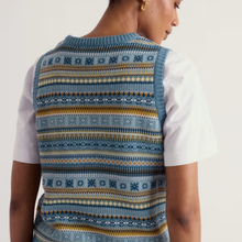 Load image into Gallery viewer, A person shown from the back wearing a sleeveless knit vest over a white short-sleeve top. The vest has a Fair Isle style pattern in shades of blue, navy, mustard yellow, and cream.
