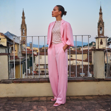 Load image into Gallery viewer, Woman in a pink suit standing on a rooftop with cityscape in the background
