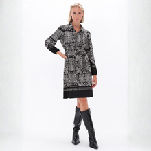 Load image into Gallery viewer, A woman modeling a long-sleeve black and white patterned shirt dress with black cuffs and a black hem, paired with black knee-high boots, against a white studio background.
