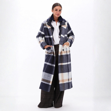Load image into Gallery viewer, A woman modeling a long navy blue plaid coat with beige, white, and gray stripes, worn over a white collared shirt and dark wide-leg trousers, against a plain white studio background.
