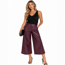 Load image into Gallery viewer, A woman modeling a pair of high-waisted, wide-leg cropped pants in a deep burgundy faux leather, paired with a black sleeveless top and black high-heeled sandals against a plain white background.
