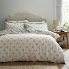 Load image into Gallery viewer, A neatly made bed in a bright bedroom setting, featuring a cream duvet cover and matching pillow shams with a repeating gray leaf pattern, plus sage green accent pillows. A wooden nightstand with a lamp and window is visible beside the bed.
